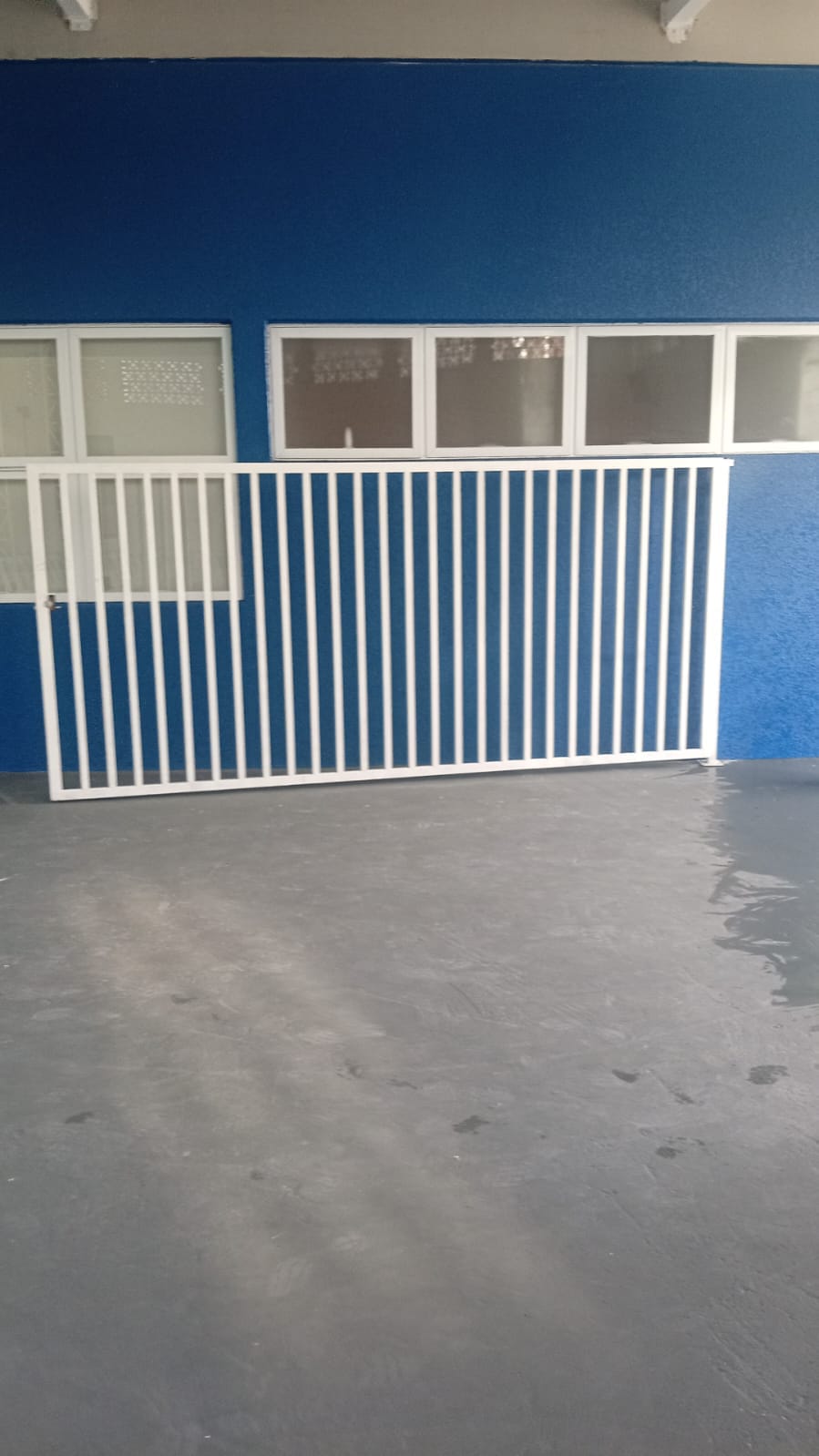 Portão branco de grades com folha de abrir em frente às janelas
