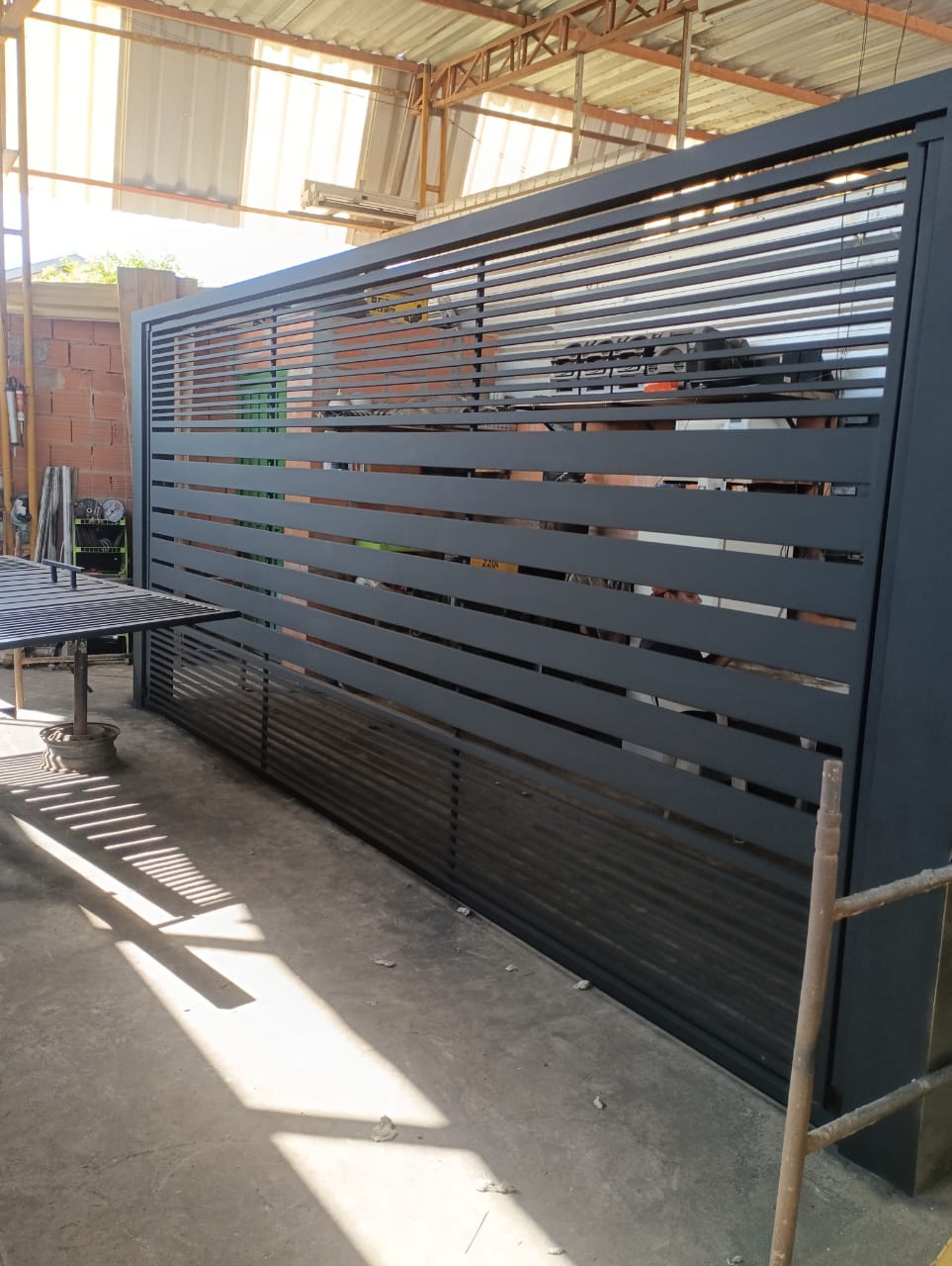 Portão de metal cinza escuro com ripas horizontais na oficina