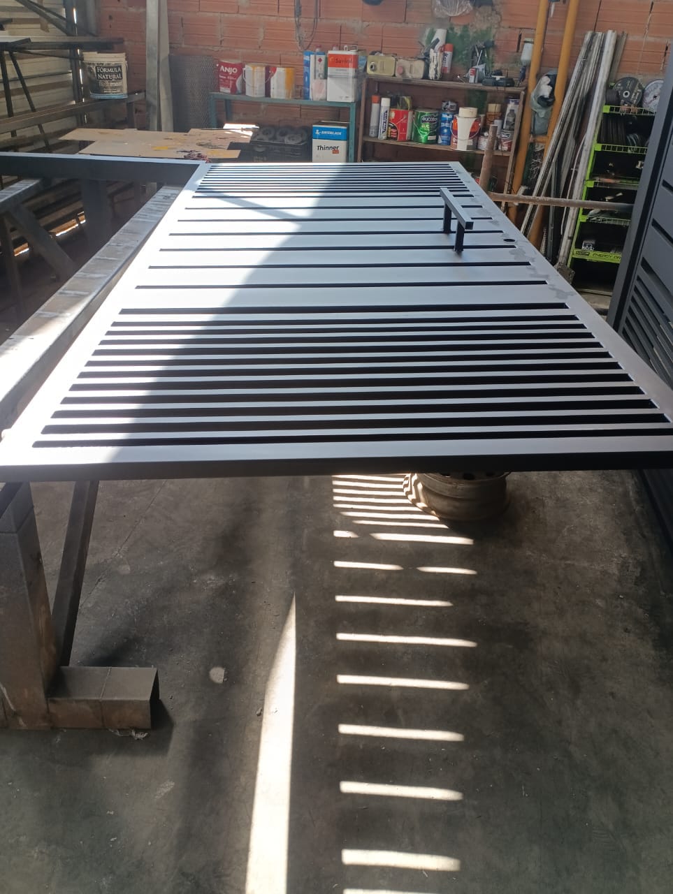 Portão de metal cinza com ripas horizontais sobre a bancada da oficina